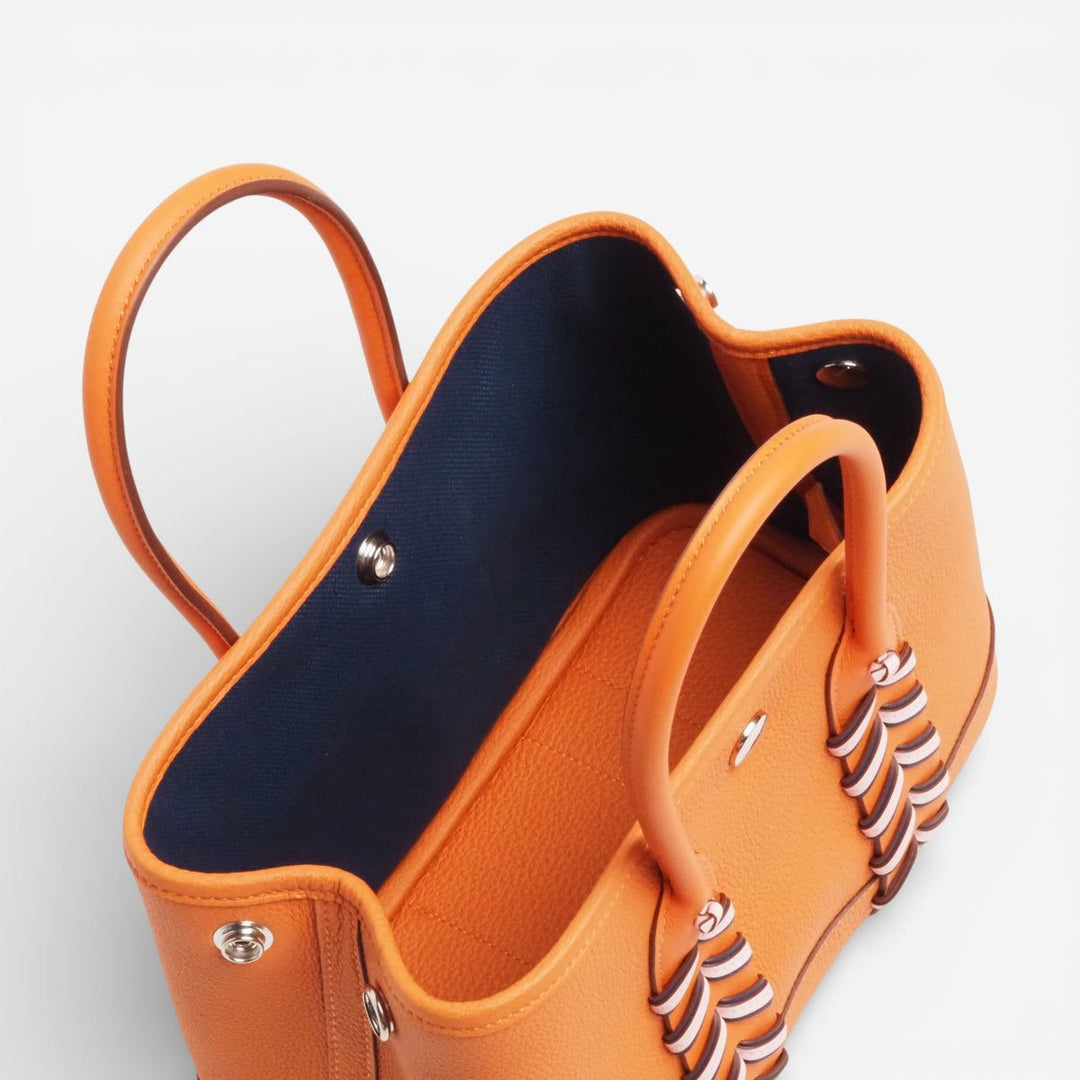 Orange handbag with decorative handles on a light gray background