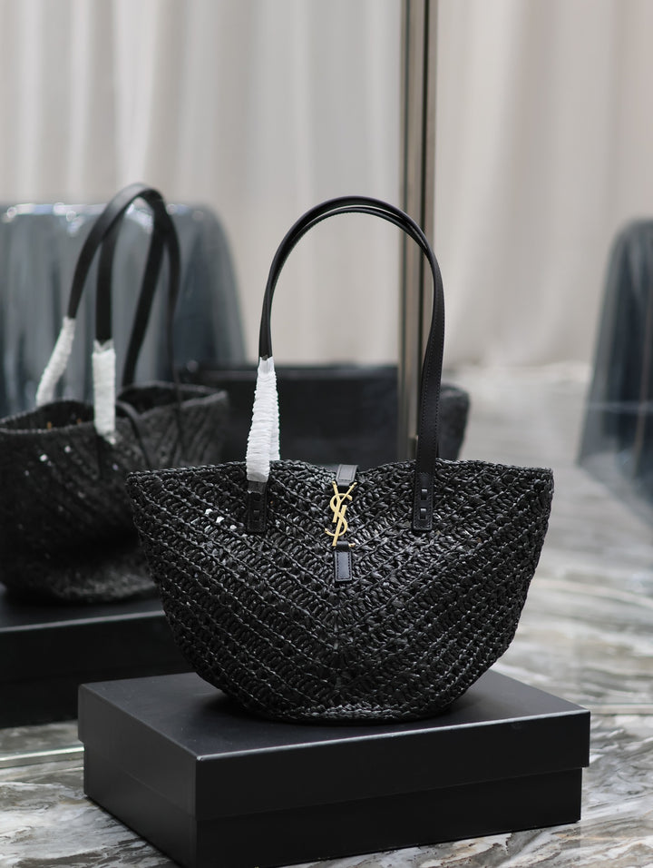 Black woven handbag with a brand logo on a black box against a neutral background