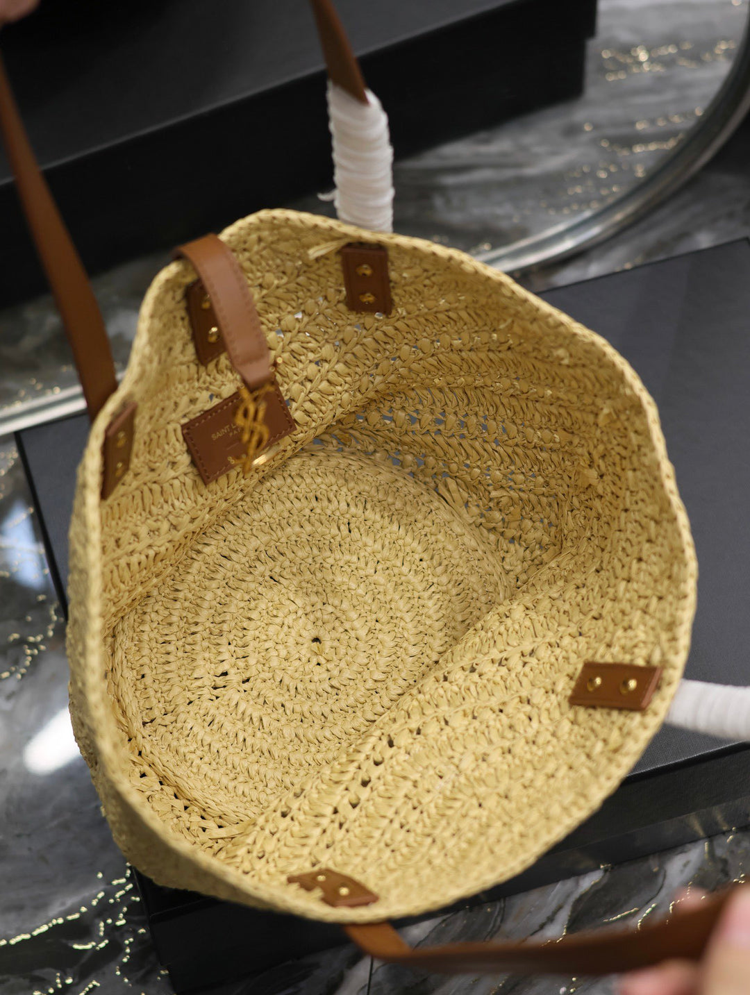 Woven straw bag with leather straps on a reflective surface