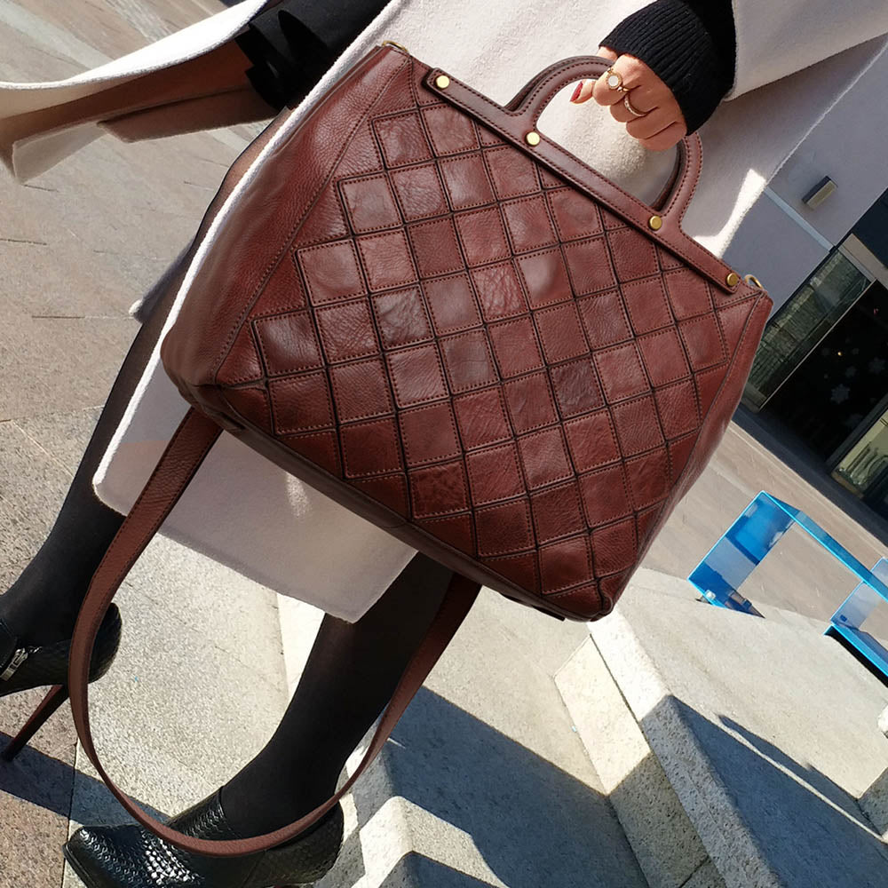 Brown woven leather handbag held by a person outdoors.
