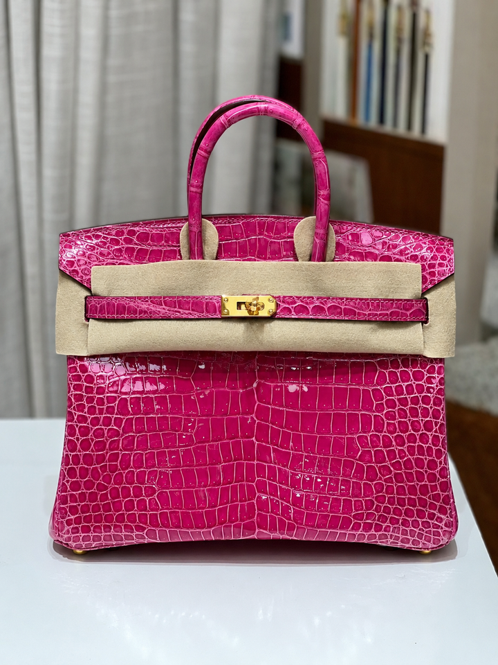 Pink crocodile skin handbag with beige leather trim on a white surface.