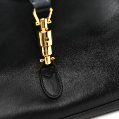Close-up of a black leather handbag featuring a polished gold-tone metal clasp and a matching black leather strap loop.