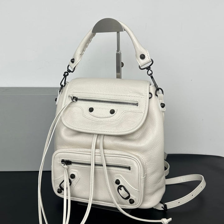 A dark brown pebbled leather backpack with multiple zippered pockets and a top handle, displayed on a stand against a white 