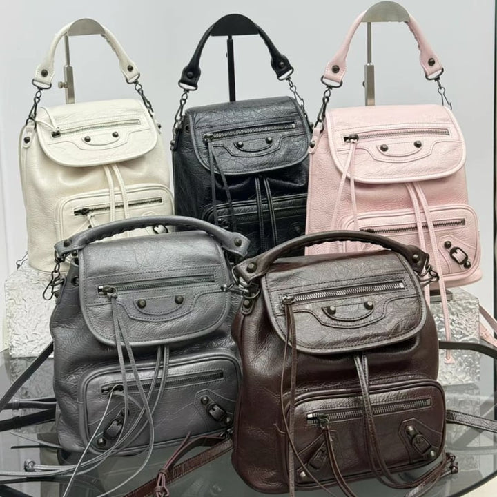 Four Balenciaga Paris mini backpacks in different colors: cream, black, light pink, gray, and dark brown, arranged on a reflective surface.