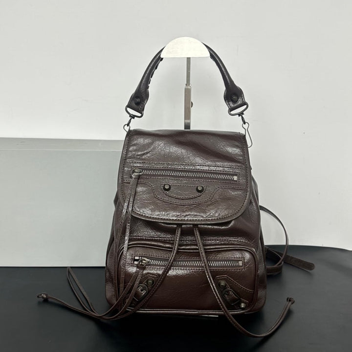 Black studded leather flap backpack product shot on dark reflective surface