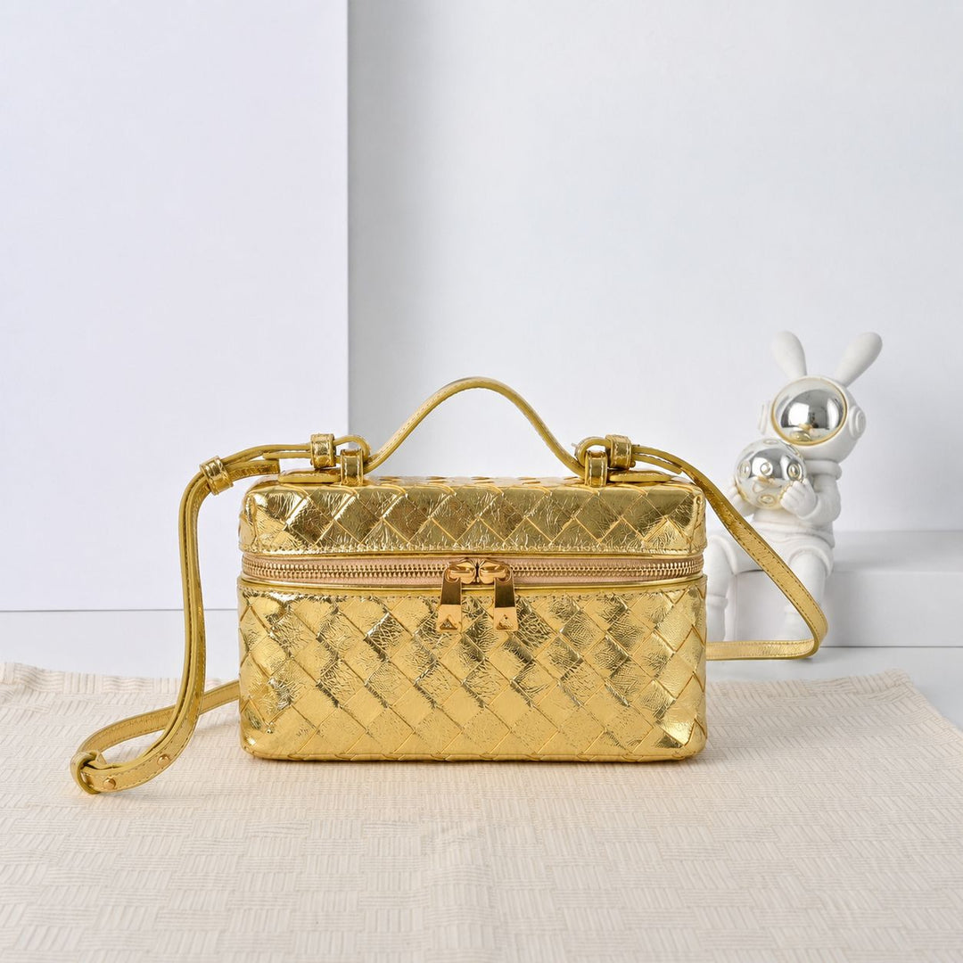 Gold metallic woven leather vanity crossbody bag with top handle on neutral linen surface