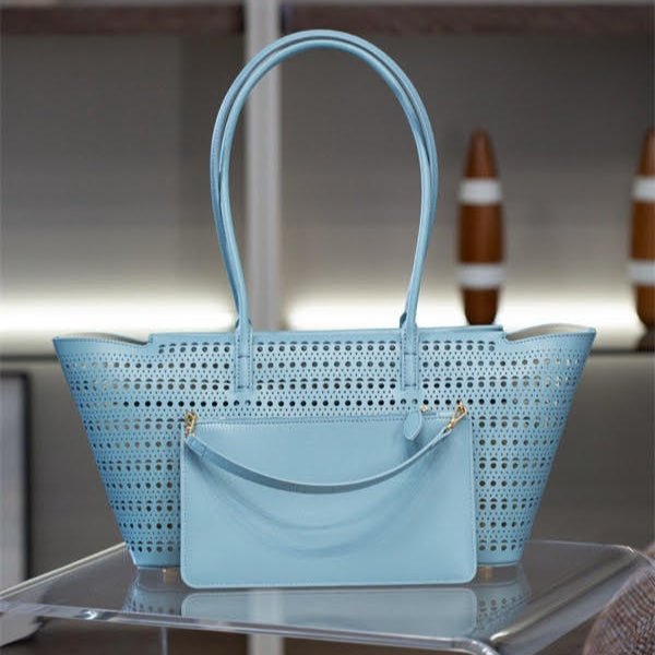 Light blue perforated handbag on a reflective surface with a blurred background